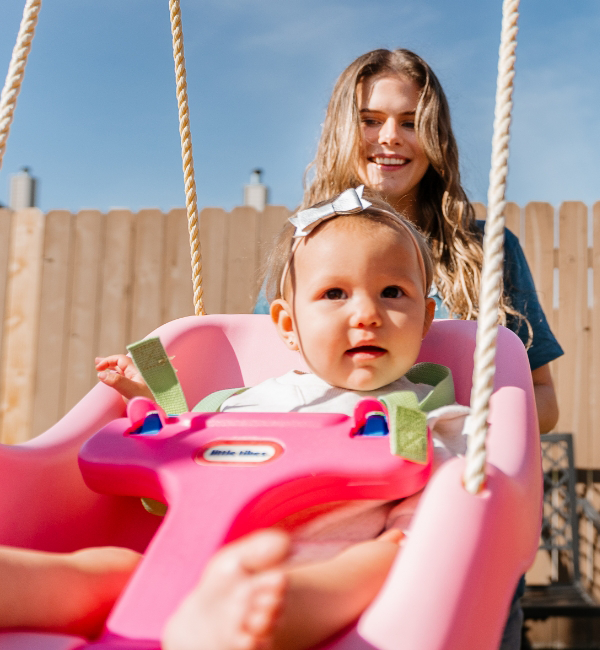 A Time Out Sitter pushing a baby girl in a swing.