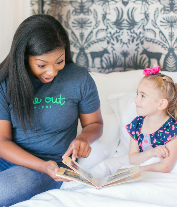 A Time Out Sitter reading a book to a young girl.
